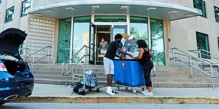 A mother and son load a wheeled cart with belongings on move-in day.