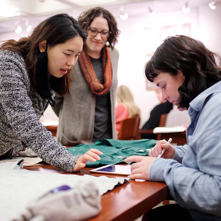 An instructor looks at two students working together on a fashion project.