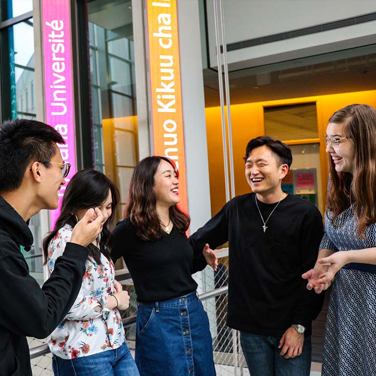 A group of five students talk and laugh together in the common area of the Hamilton Lugar School of Global and International Studies building.
