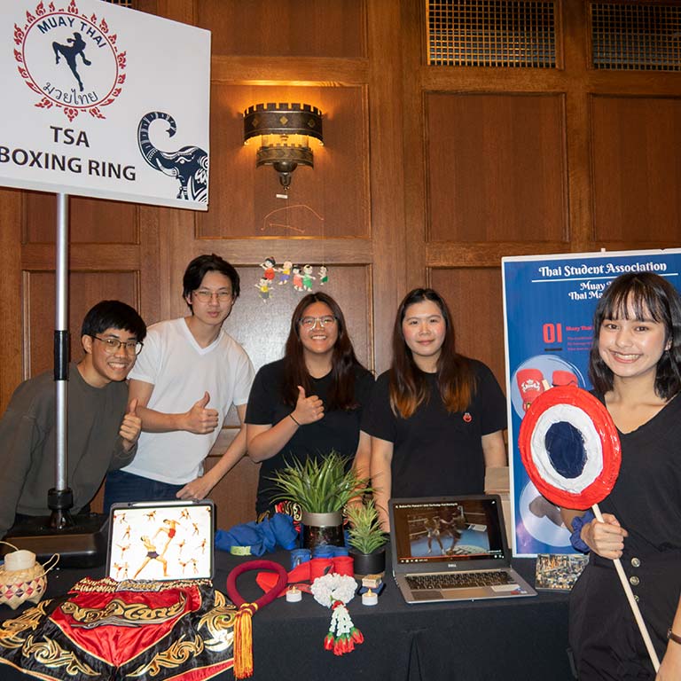 Five students pose around a table with objects displayed in relation to "Muay Thai TSA Boxing Ring."