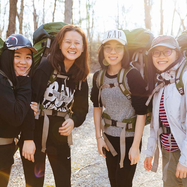 Four students wearing hiking backpacks in a wooded area