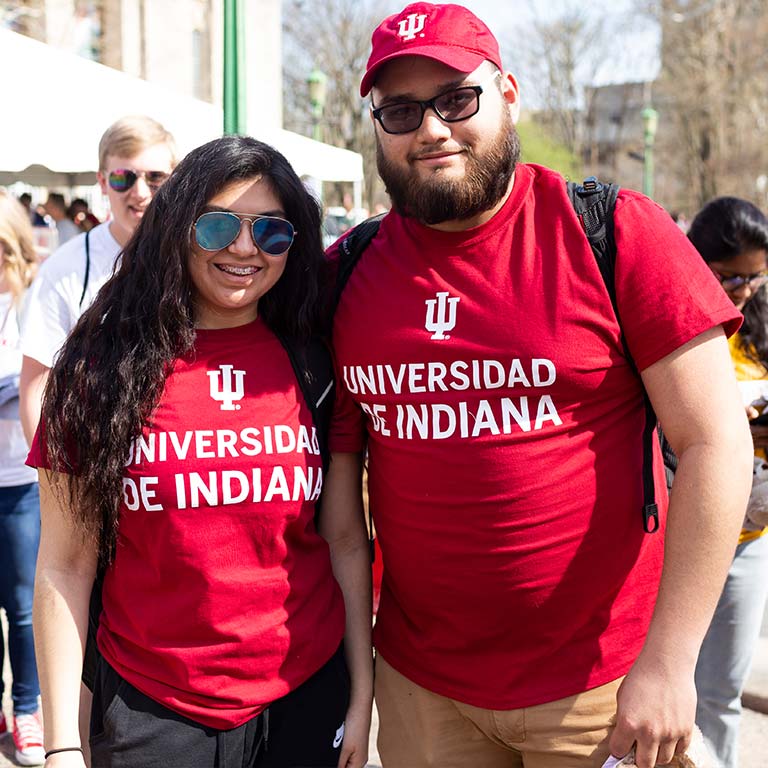 Two students stand outside at an event wearing "Universidad de Indiana" tee shirts.
