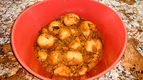 A bowl of Alu’r dom—a Bengali dish of spicy curried potatoes—sitting on a countertop.
