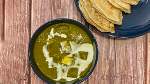 A dish of palak paneer sits on a wooden table.