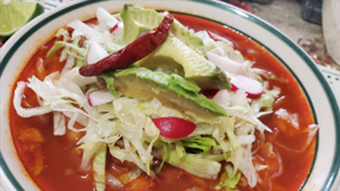 A bowl of pozole topped with cabbage and avocado.