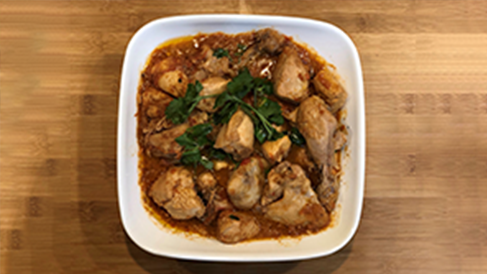 A bowl of Pakistani chicken karhai sits on a wooden tabletop.