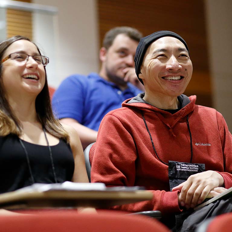 A man and woman sit in auditorium seats smiling during a presentation.